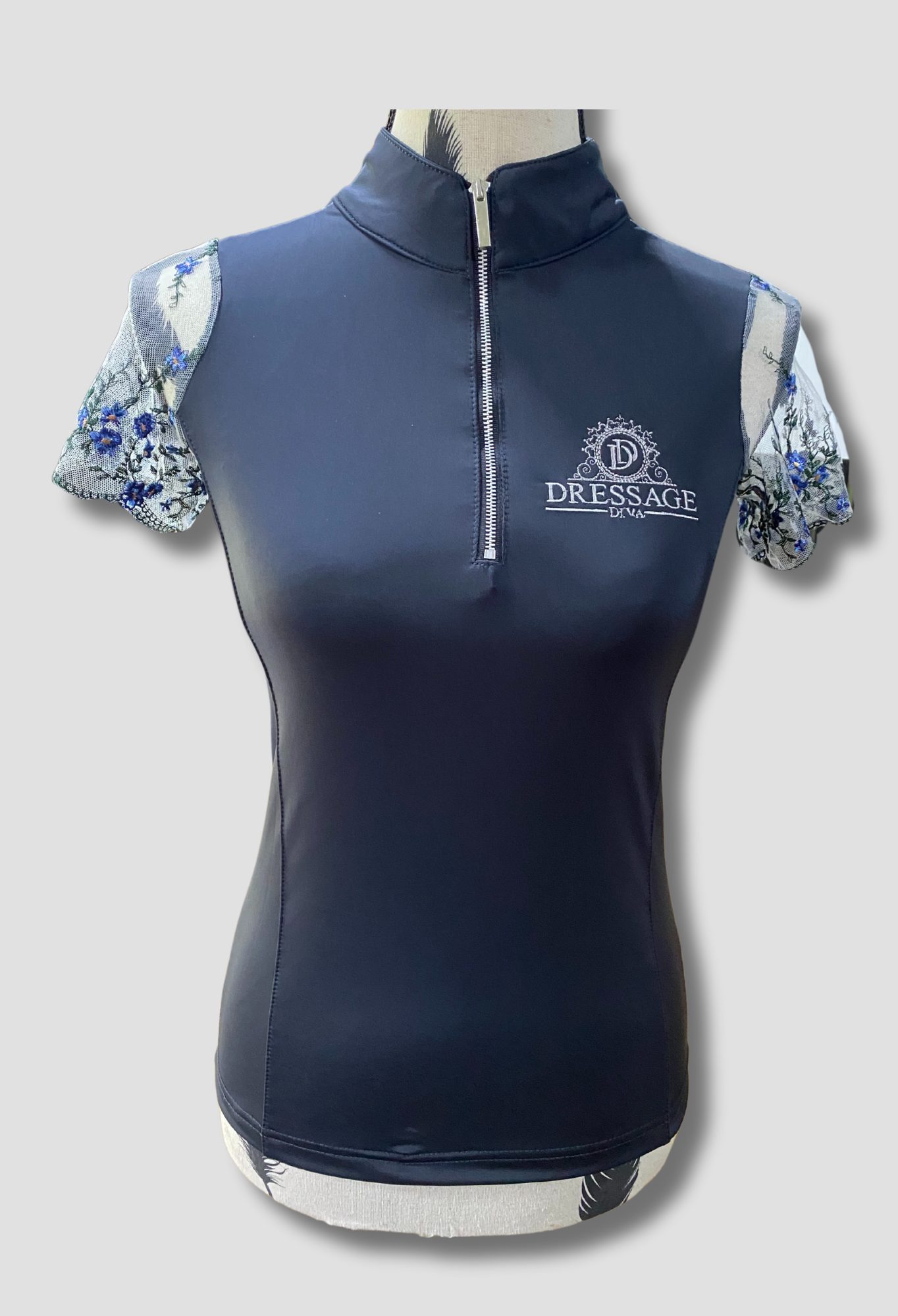 A dark grey short sleeve riding shirt with embroidered lace sleeves and a front zipper, displayed on a mannequin.